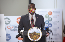 Calvin Ball at podium in front of 50+ center reopening boards