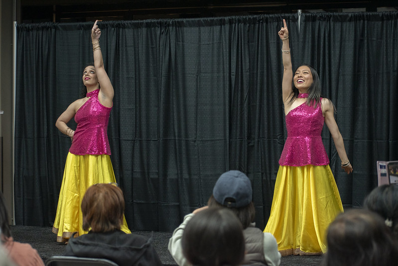 Two female bollywood dancers dressed in yellow skirts and pink shiny tops.