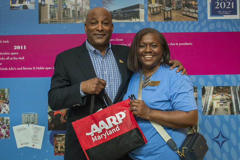 Male and female posing for a photo holding up bag that says AARP Maryland