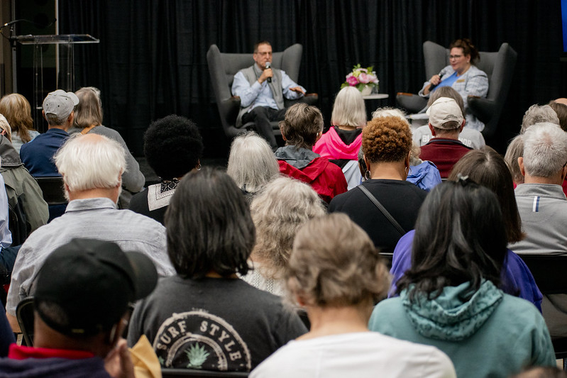 Audience members back of heads facing stage with keynote speaker and administrator.