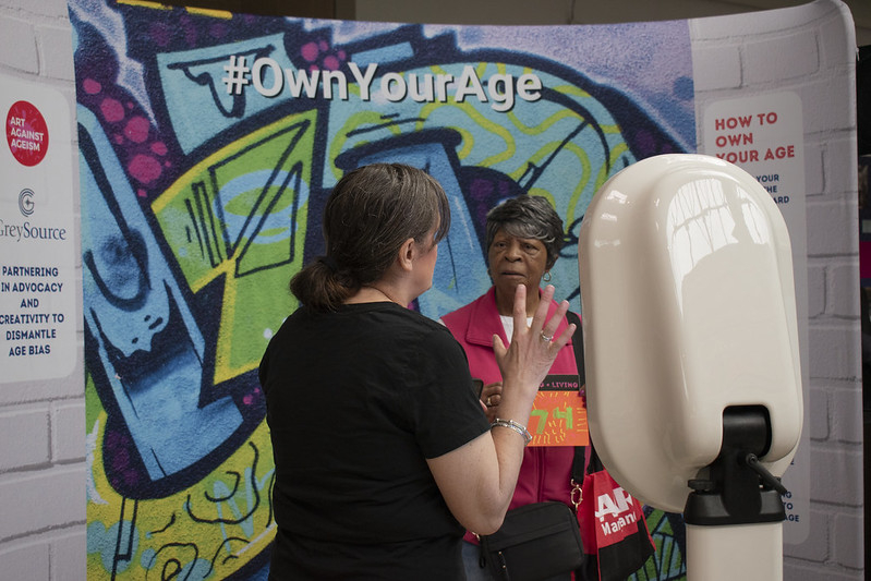 Woman at the Own Your Age Photobooth being helped by the vendor.