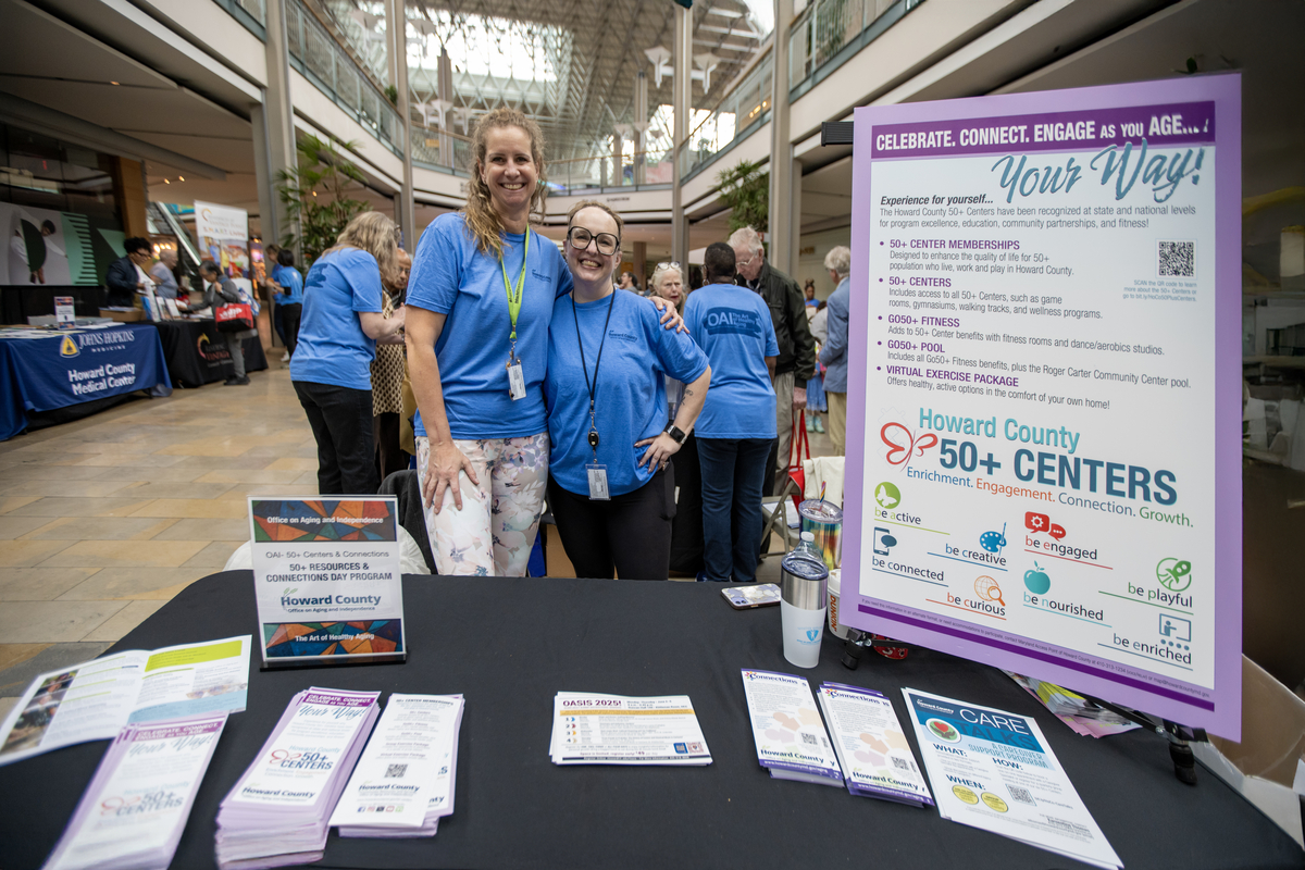 Two female white staff member posing for a photo at the 50+ Center table at the event
