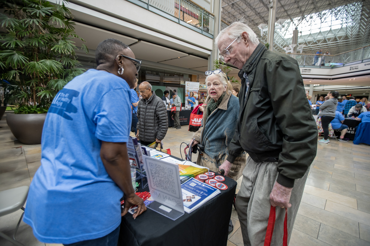OAI female staff member speaking to two older adults at booth at the event.