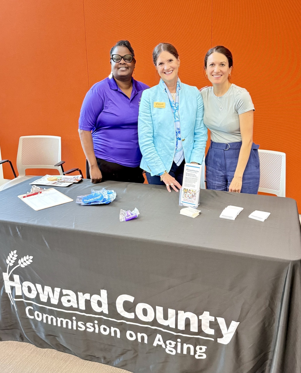 Three female commission on aging members posing together at resource table that says howard county commission on aging.