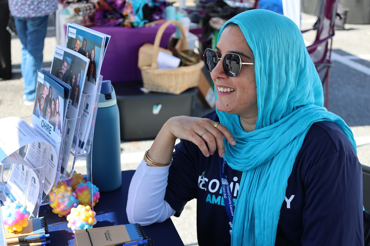 A woman in a blue hijab smiles while speaking to a community member.