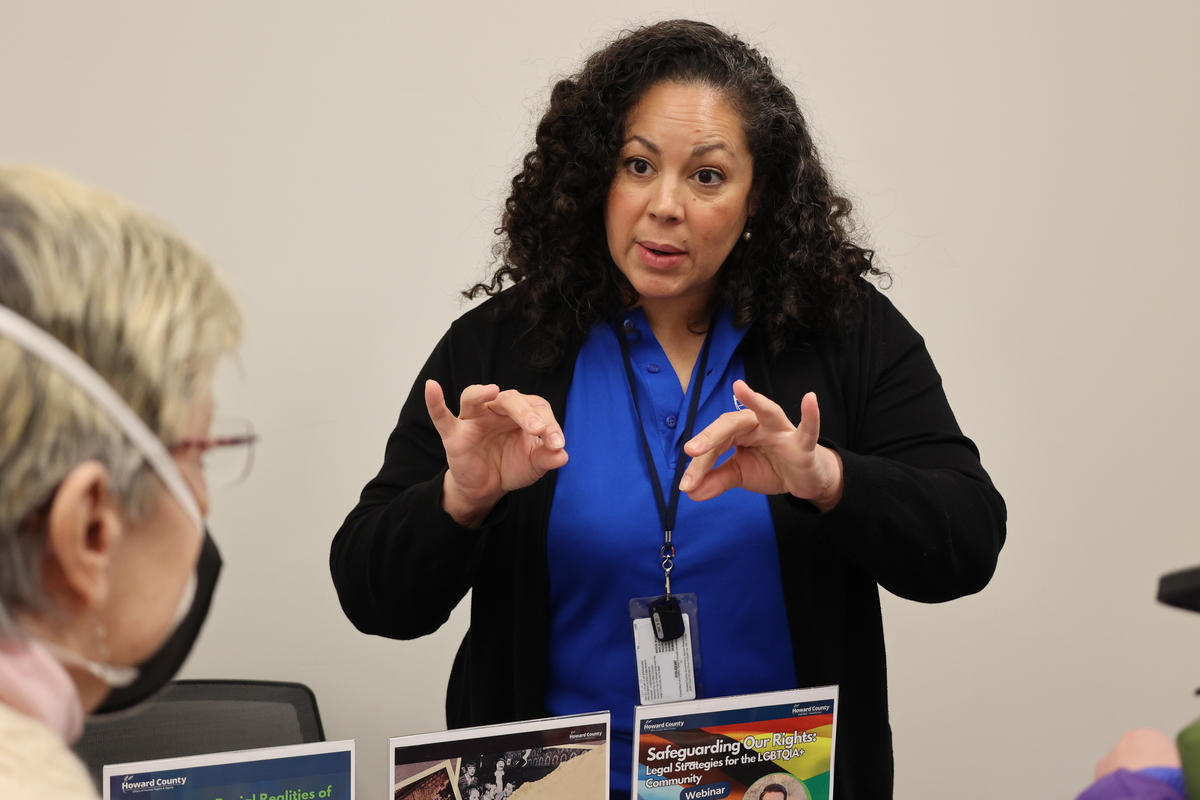 A woman with curly, shoulder-length hair speaks to a community member.