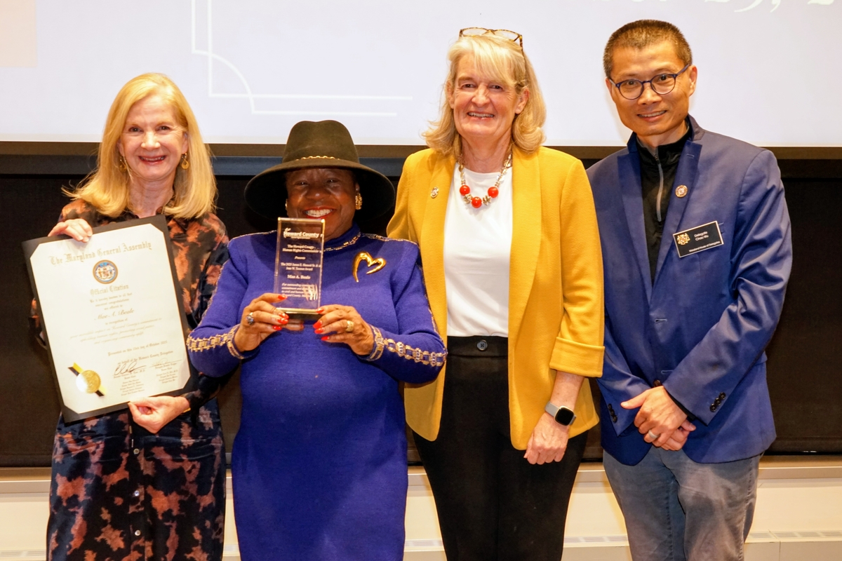 4 people in business formal dress stand in front of a projection reading "2025 Human Rights Commission Awards Ceremony"