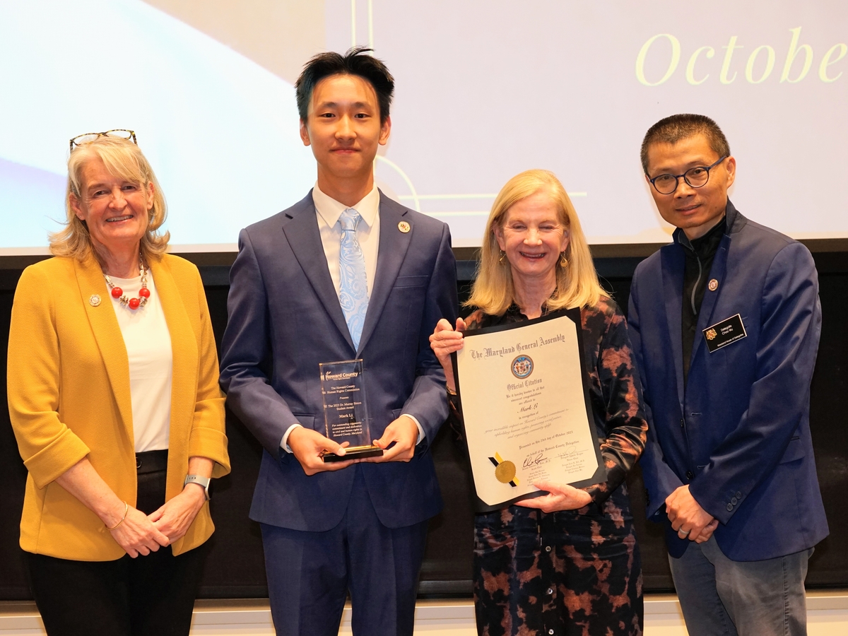 4 people in business formal dress stand in front of a projection reading "2025 Human Rights Commission Awards Ceremony"