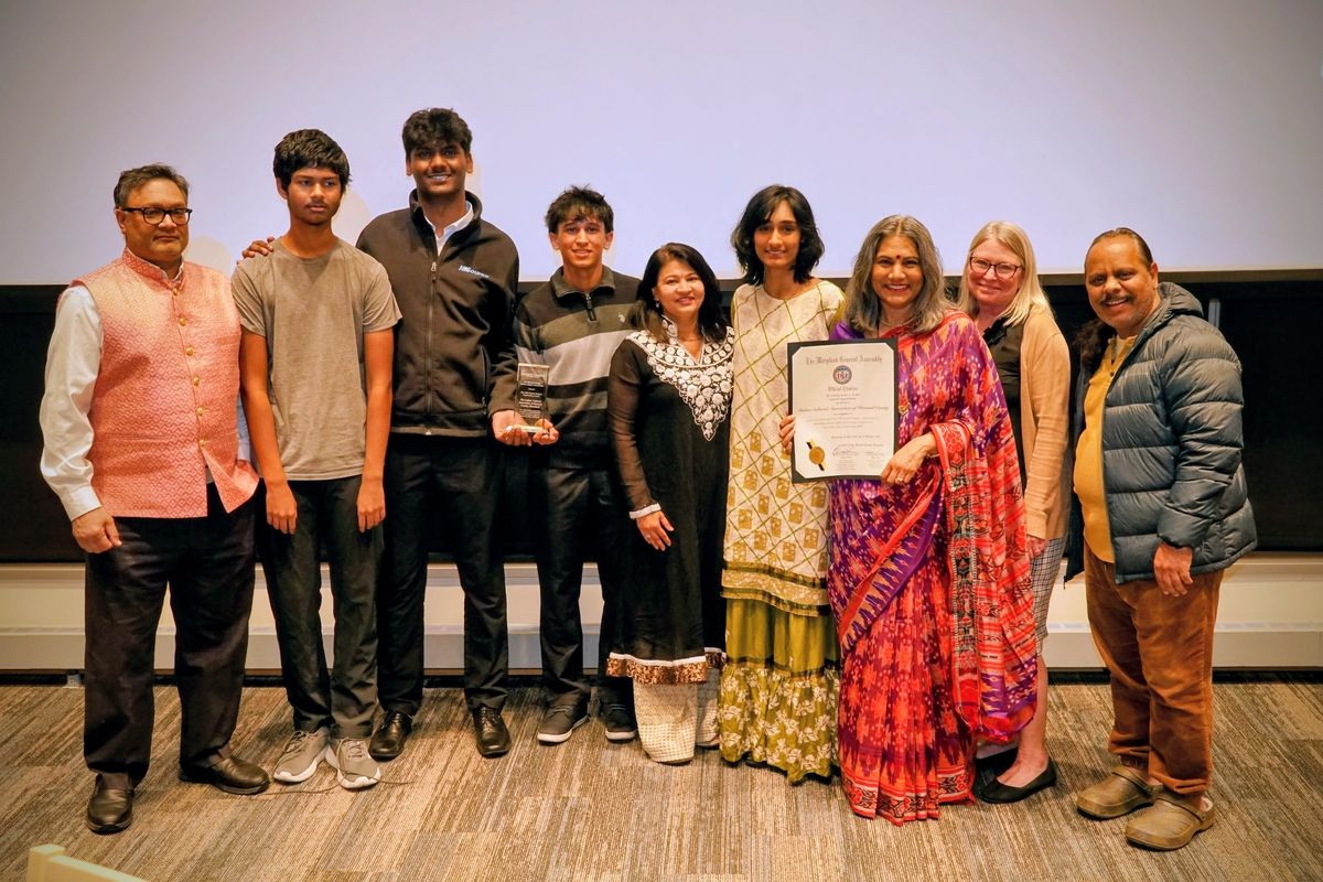 9 people in business formal dress stand in front of a projection reading "2025 Human Rights Commission Awards Ceremony"