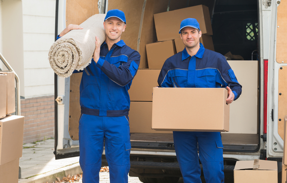 Two moving men holding a rug and a box in front of a moving truck