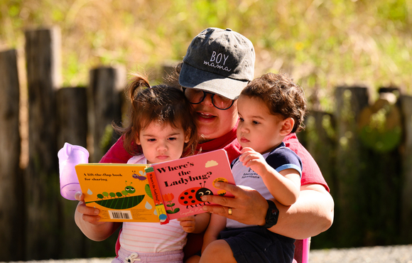 Two toddlers getting read a book by their mother. 