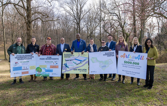 A photo of County Executive and attendees holding up signs outlining his proposed Fiscal Year 2026 budget investments for Elkridge.