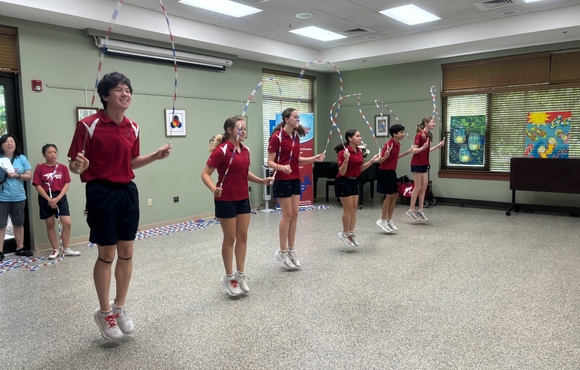6 kids dressed in maroon shirts and black shorts doing a jump rope routine