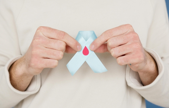 Caucasian person holding up light blue ribbon with blood droplet in their hands. No face shown.