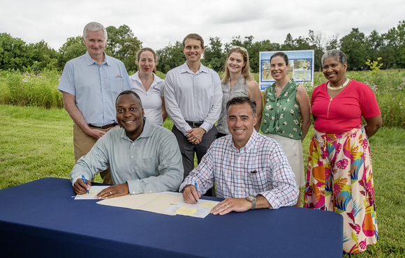 A photo of County Executive Calvin Ball and Columbia Association (CA) President and CEO Shawn MacInnes getting read to sign a Memorandum of Understanding to enhance collaboration between the County and CA and strengthen local action on climate and energy independence.