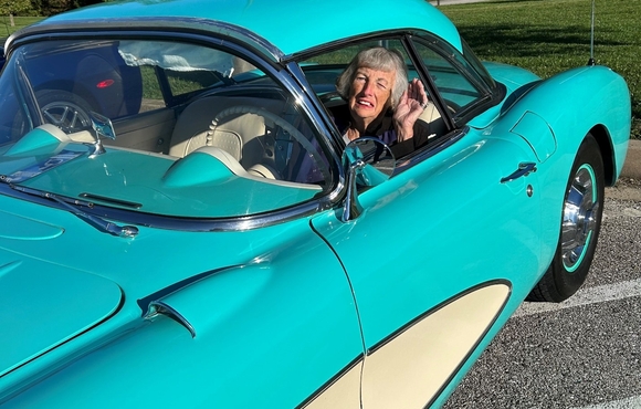 Older white woman sitting in the driver seal of a teal and cream colored classic car.
