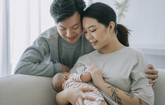 Asian Chinese young mother breastfeeding baby girl at home with father