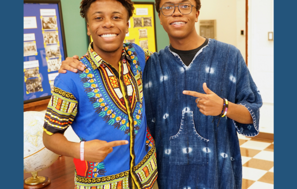 Two young people in traditional African clothing smile at the camera. 