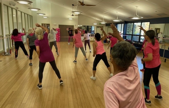 Women doing a zumba class dressed in pink with backs facing the camera.