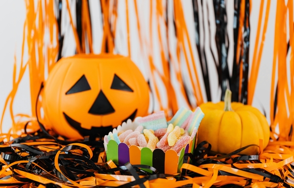 Pumpkin, plastic jack-o-lantern and cup of candy sitting atop black and orange streamers.