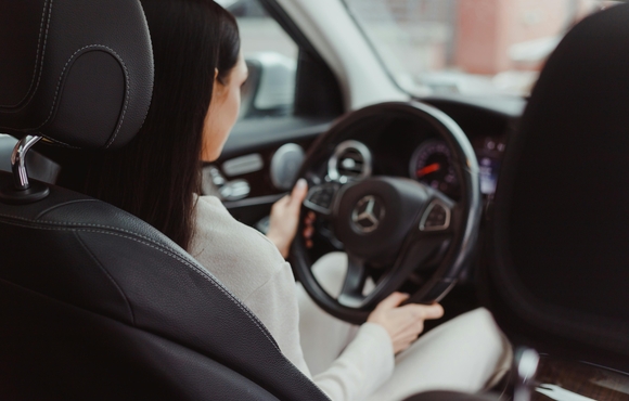 Inside view of woman driving car with hands on steering wheel.