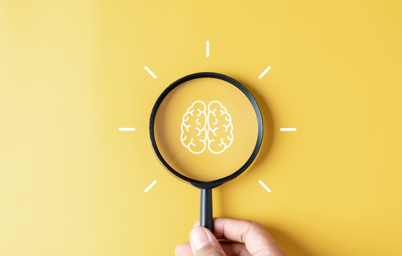 Drawing of a brain with a magnifying glass over top on a bright yellow background.