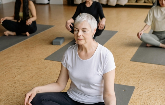 Older woman with white hair and glasses looking at a photo album on a couch with a younger woman with blonde hair.