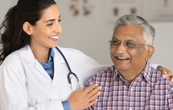 An older man with light brown skin is seen by a smiling doctor with long brown hair. 