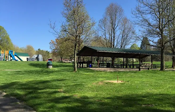 Wide shot of park with a picnic pavilion, blue sky, and green grass