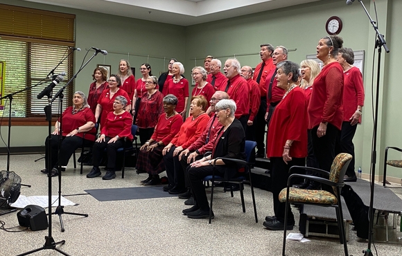 Group of about 25 older adult men and women all wearing red performing songs