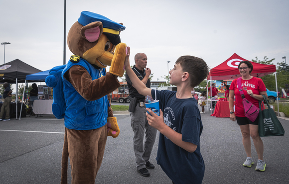A person dressed as Chase from Paw Patrol high fives a child at National Night Out