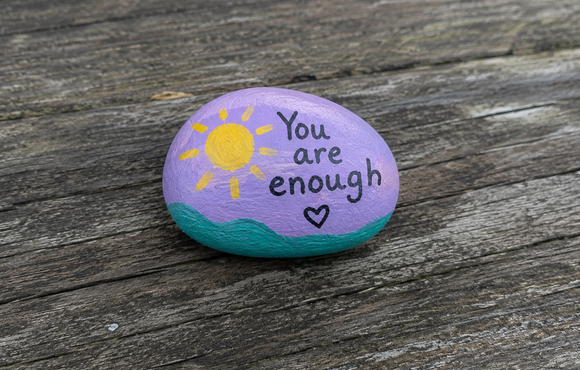 Rock painted with "You are enough". Also includes a sun and a heart.