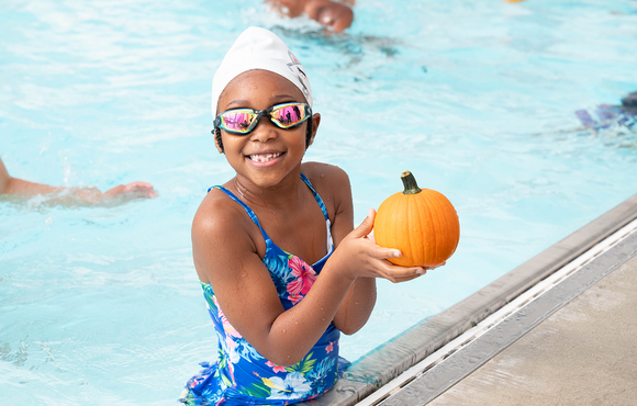 Smiling girl looking at camera holds pumpkin near edge of pool