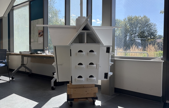 white 3-story birdhouse sitting by a window in a workspace