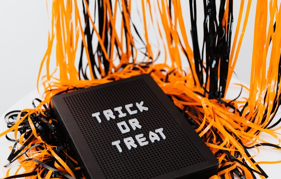 orange and black streamers behind a black board with white writing that says "Trick or Treat"