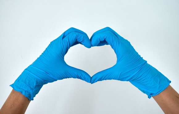 two blue-gloved hands form a heart shape in front of a white background