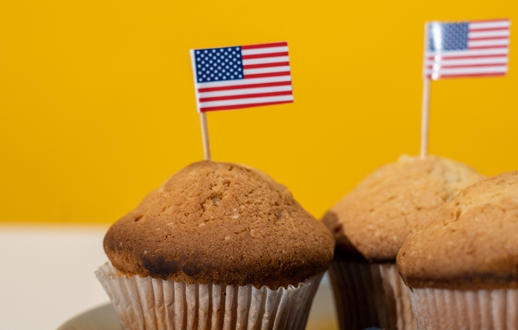 American flags on toothpicks sticking out of muffins surrounded by blueberries on a blue plate