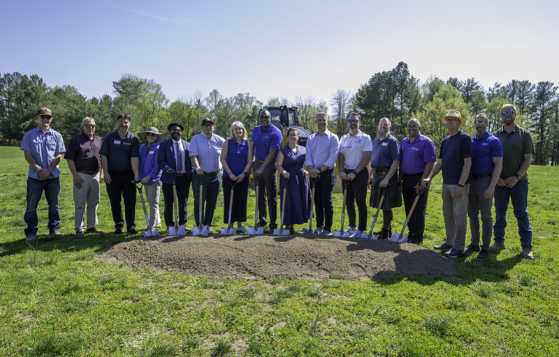 County Executive Calvin Ball with Department of Recreation & Parks employees and other community members posing with shovels in hand and a mound of dirt in front of them outside before digging into the ground to ceremoniously break ground on Cradlerock Park in Columbia.