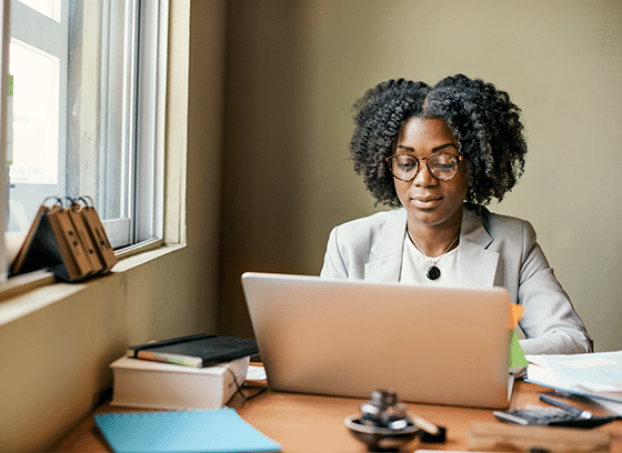 A woman sitting by a window, typing something on a laptop