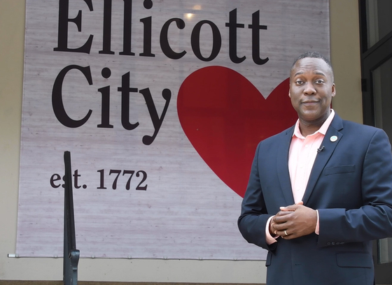 County Executive Calvin Ball featured alongside a sign that reads "Ellicott City, established 1772" with a red heart to the right.
