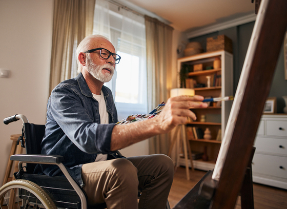 Older adult in wheelchair paints in his house 