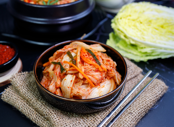 A bowl of kimchi on a burlap napkin with chopsticks and napa cabbage nearby