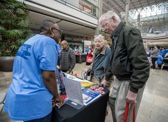 OAI black female staff member assisting two older adults, one male and one female, at a table at an event.