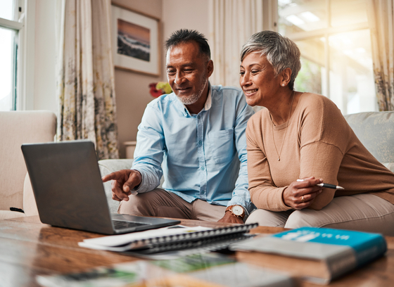 Two older adults, one male and one female looking at a laptop together on the couch.