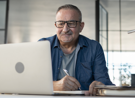 Older adult male with glasses looking at a laptop.