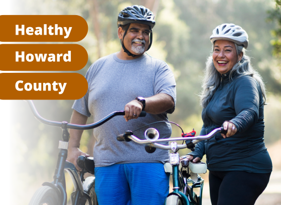 Man and women smiling, wearing bike helmets and holding bike outside. Text on orange background: Healthy Howard County
