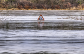 In a stormwater pond, the water level approaches a 'no swimming' water hazard sign.