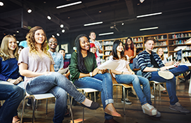 A group of students in a library, listening to a presentation