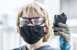 masked woman holding up a rock
