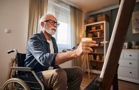 Older adult in wheelchair paints in his house 